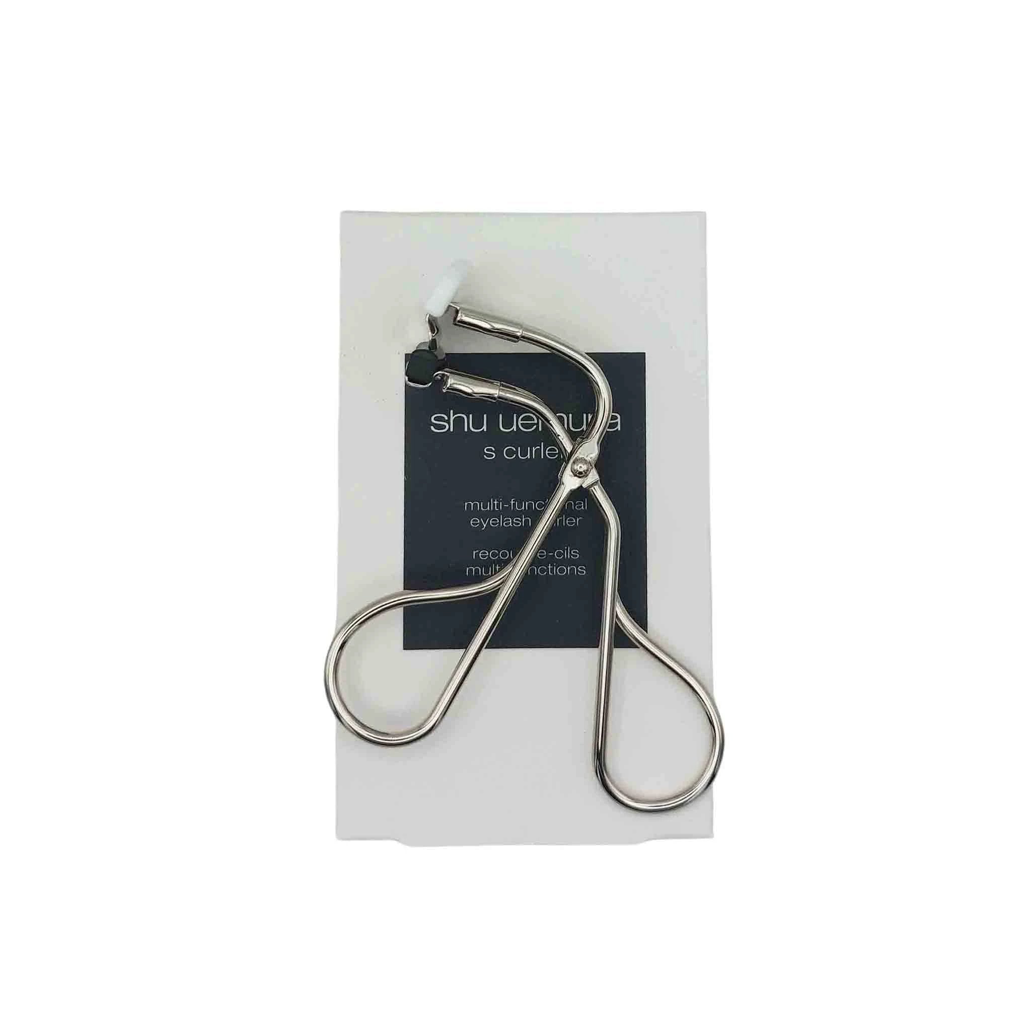 Shu Uemura S Curler, silver metal eyelash curler with white silicone pad, displayed over a dark card.